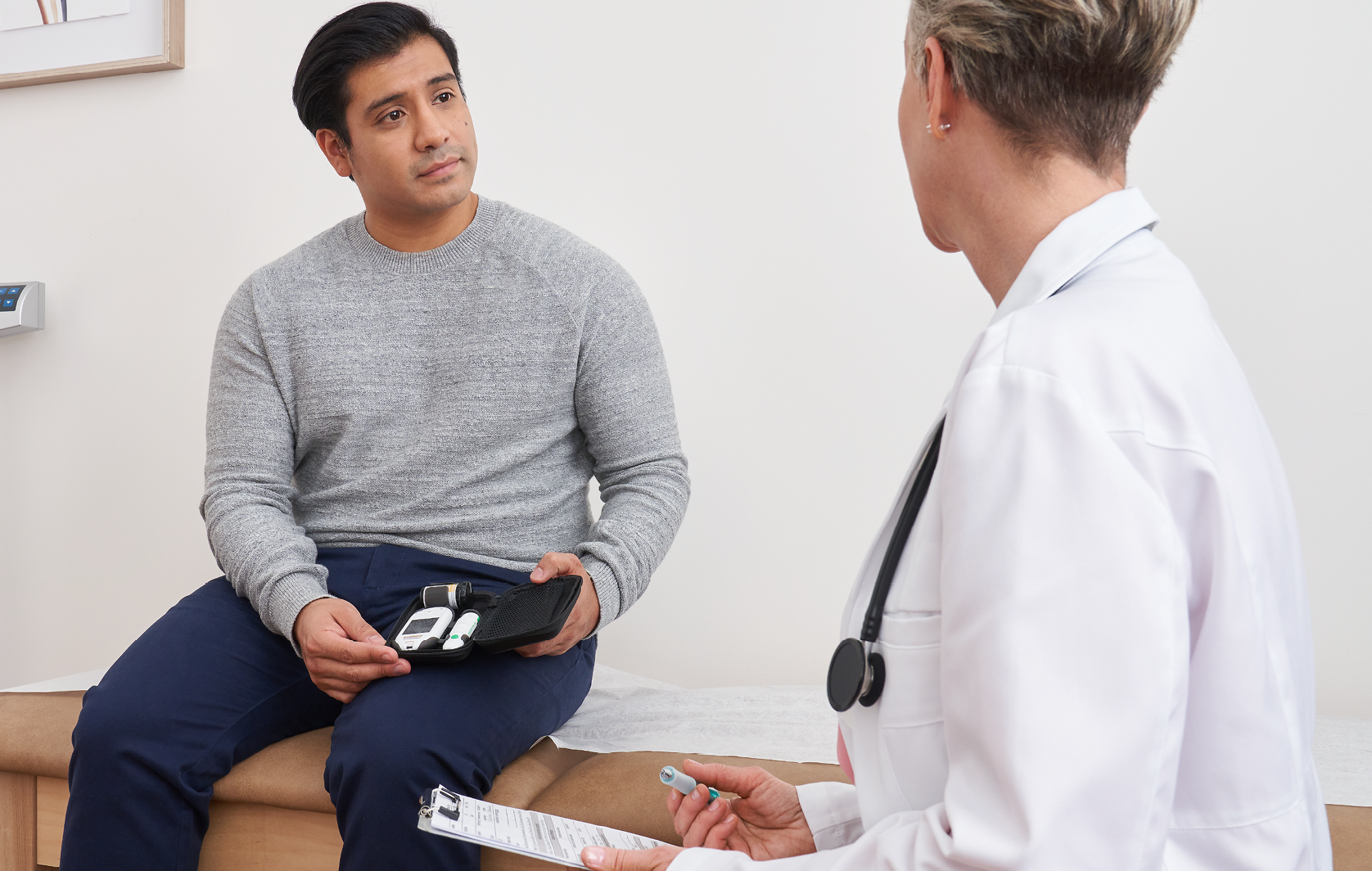 Paciente em consulta médica segurando um medidor de glicose e caneta de insulina.