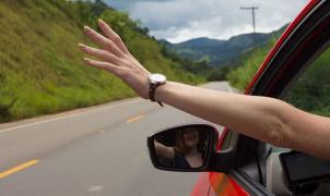 Um braço para fora da janela de um carro em movimento numa estrada rural.