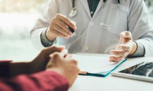 Médico de bata branca a discutir um relatório com um paciente, mostrando um documento numa pasta.