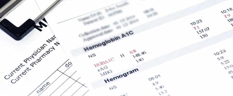 Primeiro plano de resultados de exames de laboratório mostrando os valores de hemoglobina glicada e hemograma numa folha.