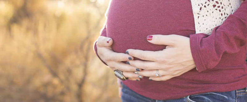 Mulher grávida de camisola vermelha a tocar na barriga.