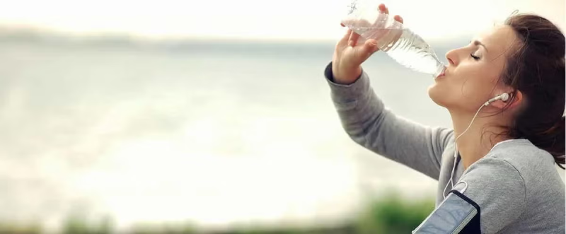 Pessoa a beber água de uma garrafa após fazer exercício.
