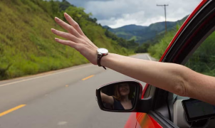 Um braço para fora da janela de um carro em movimento numa estrada rural.