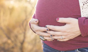 Mulher grávida de camisola vermelha a tocar na barriga.