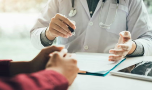 Médico de bata branca a discutir um relatório com um paciente, mostrando um documento numa pasta.