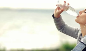Pessoa a beber água de uma garrafa após fazer exercício.